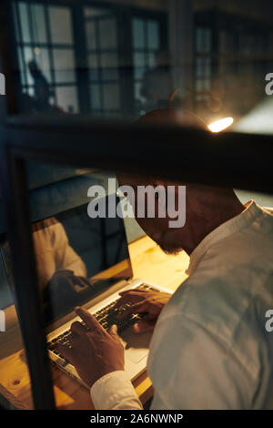 Black businessman working on laptop overtime in dark room all night long to complete project within deadeline Stock Photo