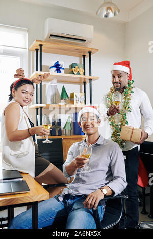 Group of cheerful colleagues posing with glasses of champagne when having small Christmas party in office Stock Photo