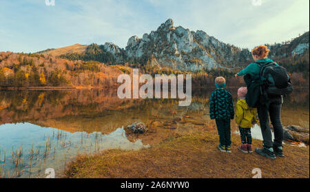 Mum and kids at the shore of the Laudachsee, Austria, with the stunning Katzenstein rising in the background and reflecting in the crystal clear water Stock Photo