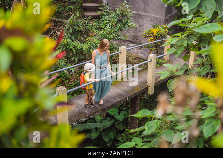 Mother and son tourists in Bali walks along the narrow cozy streets of Ubud. Bali is a popular tourist destination. Travel to Bali concept. Traveling Stock Photo