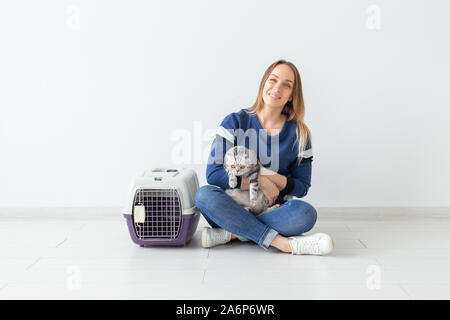Charming positive young woman holds in her hands her beautiful gray fold scottish cat sitting on the floor in a new apartment. Pet concept. Stock Photo