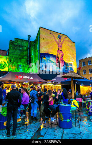 People eating, drinking and socialising at the Lower Marsh Market near Waterloo, mural on the wall of Cubana Restaurant & Cocktail Bar, London, UK Stock Photo