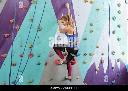 Young active female in sportswear holding by multi-color rocks on climbing wal Stock Photo