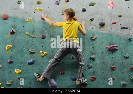 Back view of active schoolboy in sportswear moving upwards along climbing wall Stock Photo