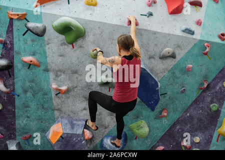 Rear view of young sportswoman grabbing by small rocks on climbing wall Stock Photo