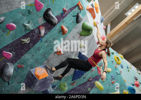 Active girl holding by one of small rocks throughout climbing equipment Stock Photo