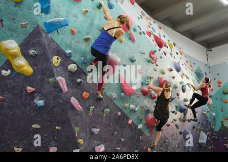 Three young sporty women in activewear grabbing by rocks on climbing equipment Stock Photo