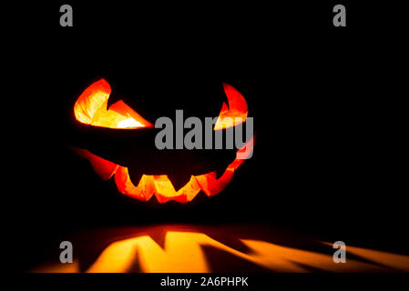 Halloween pumpkin smile and scary eyes for party night. Close up view of scary Halloween pumpkin with eyes glowing inside at black background. Selecti Stock Photo