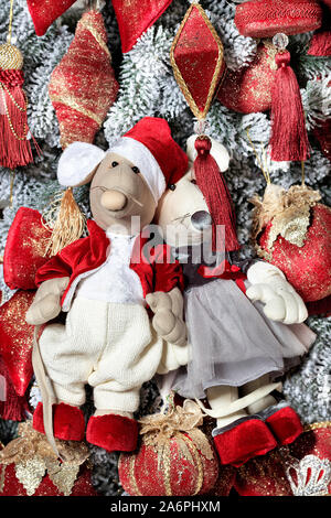 Little decorative toy mice is festively dressed in red clothes for the eve of the rat year on the background of the New Year tree, close-up view. Stock Photo