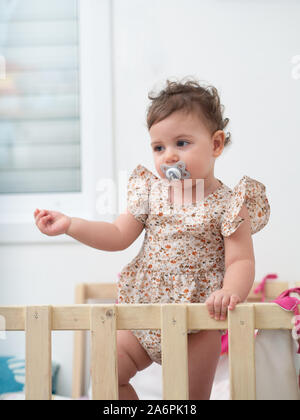 1 year old baby girl stands in her cot (or crib) Stock Photo