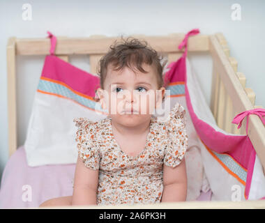 1 year old baby girl stands in her cot (or crib) Stock Photo