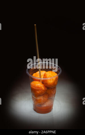Kwek – Kwek / Tokneneng – a Filipino  tempura-like street food in plastic cup with stick in  black isolated background. Stock Photo