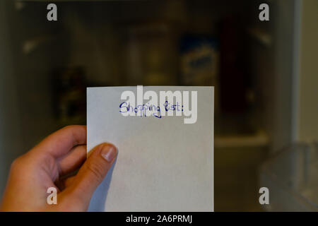 Hand holding a shopping list in front of a fridge. Stock Photo