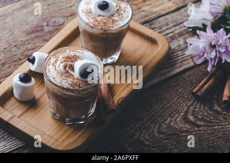 Happy Halloween monster, pumpkin spice latte with whipped cream and big marshmallow eye on top, Halloween dessert in glasses Stock Photo