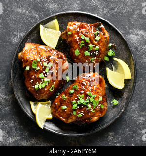 Close up of soy honey grilled chicken thighs on plate over dark stone background. Tasty food in asian style. Top view, flat lay Stock Photo