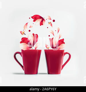 Two red mugs with red white flying flowers and petals of Amaryllis flowers standing on white background. Creative couples concept. Romantic holiday la Stock Photo