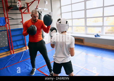 young instructor showing a boy how to defense himself, man teaching the secrets of kickboxing Stock Photo