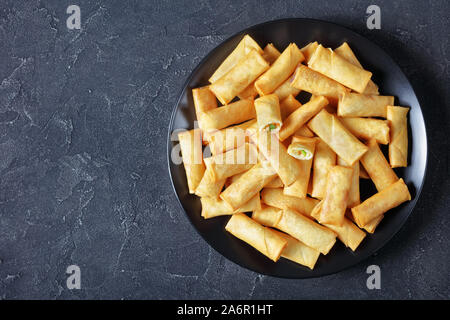 deep-fried crispy chinese spring rolls with cabbage, carrots and green peas fillings on a black plate on a concrete table, view from above, flatlay, f Stock Photo
