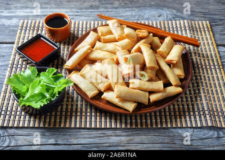 crispy bite-sized chinese spring rolls with cabbage, carrots and green peas fillings on a  plate on a rustic wooden table with sauces on a bamboo mat, Stock Photo