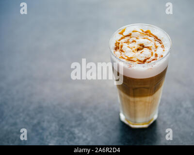 Hot latte macchiato coffee with caramel on dark tabletop with negative space for design. Natural daylight. Copy space for text. Stock Photo