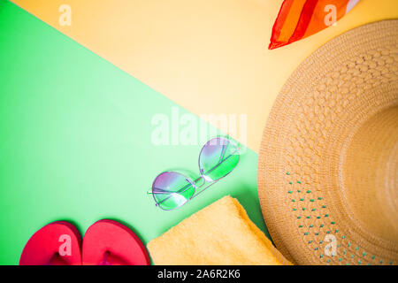 Sunglasses, towel, bright pink flip flops on light yellow and green background. Top view, copy space for text. Beach accessories, summer, holiday. Stock Photo