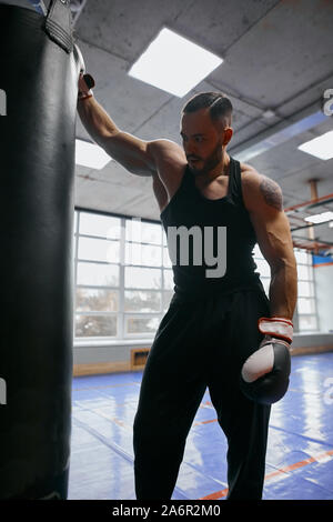 Close up portrait of a handsome young muscular man looking tired leaning on black punching bags.close up photo. tiredness concept Stock Photo