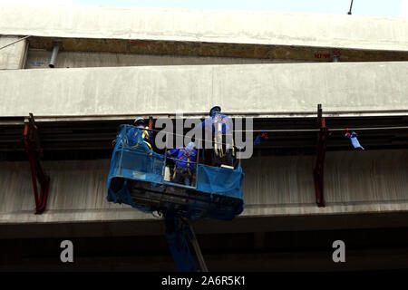 QUEZON CITY, PHILIPPINES – OCTOBER 15, 2019: Road construction workers on a basket crane work underneath a flyover. Stock Photo