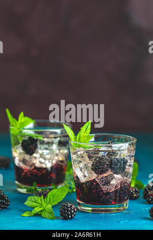 Cold summer berry drink with blackberries. Refreshing summer drink with syrup, blackberry and ice on dark blue concrete background Stock Photo