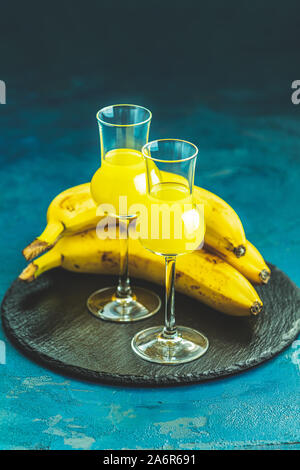 Banana flavoured liqueurs, which French call creme de banana, in  grappas wineglass on dark blue concrete surface. European aperitif drink. Selective Stock Photo