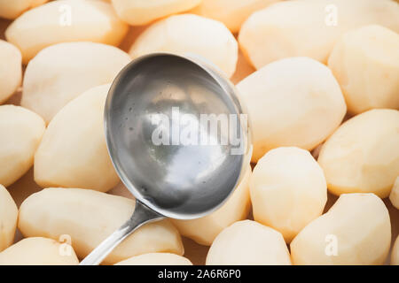 Ladle lays on raw peeled potatoes, close-up photo with soft selective focus Stock Photo