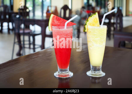 Watermelon and pineapple shakes closeup, sliced fruits pieces, straw, two fruit shakes with garnish in transparent glasses on table in bar, cold drink Stock Photo