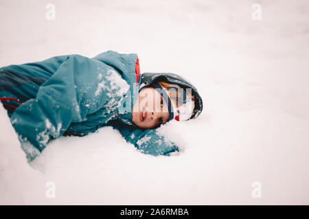 Thoughtful boy lying in snow during winter