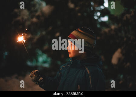 Boy holding sparkler while standing outdoors in winter Stock Photo