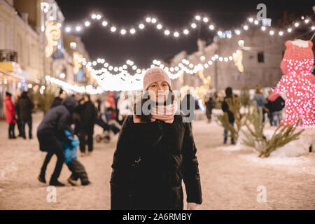Young woman wearing warm clothing standing in brightly lit street