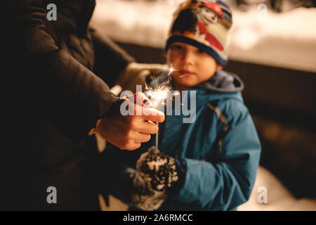 Mother igniting sparkler held by her son outdoors in winter Stock Photo