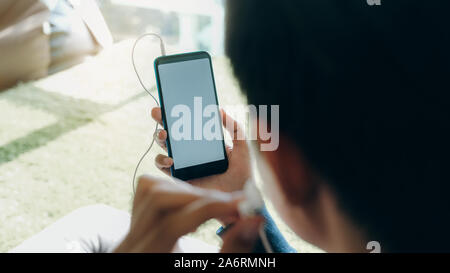 A young man lying down on a soft cushion feel relaxed and listen to online music from mobile phone in his house Stock Photo