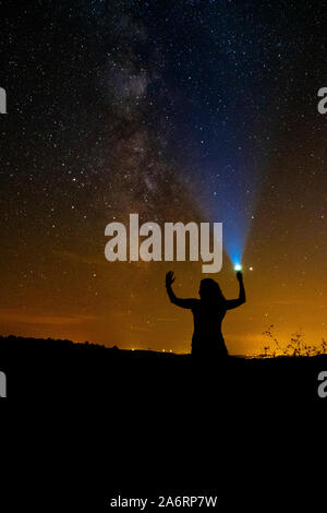 milky way photograph on a summer night. a clear sky full of stars.a woman raises her arms and with her flashlight illuminates the sky. Stock Photo