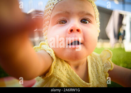 Cute baby girl in yellow reaching camera in sunny day outdoors. Stock Photo