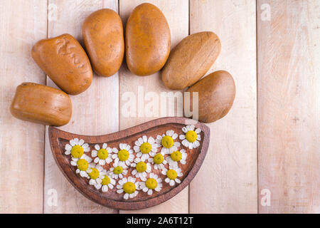 small brown stones and chamomile flowers on the table Stock Photo