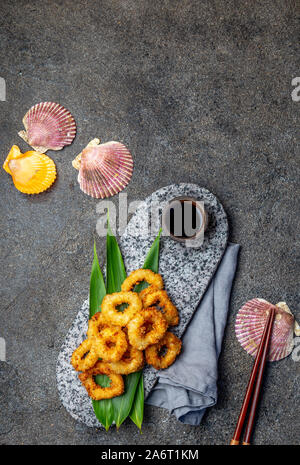 Fried squid rings on stone plate decorated with tropical leaves. Asian food concept, soy sauce and chopsticks Stock Photo