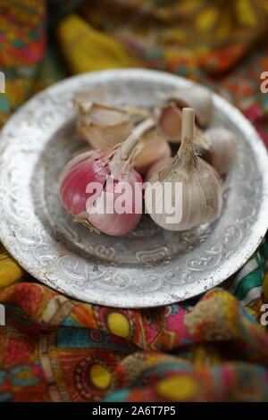 Garlic bulbs with cloves on a silver plate and vintage cloth. Stock Photo