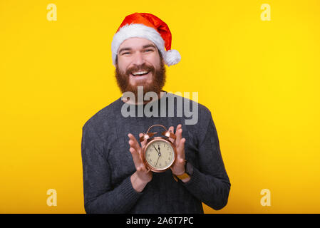 Man in santa claus hat holding alarm clock over yellow background Stock Photo