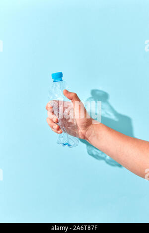 Empty plastic bottle crushed by hand on a pastel blue background with transparent shadows. Place for text. Ecological problem of environmental polluti Stock Photo
