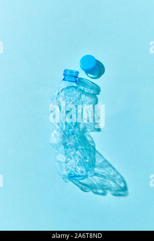 Crumpled plastic bottle with shadows on a pastel blue background. Concept enviroment pollution of plastic. Stock Photo