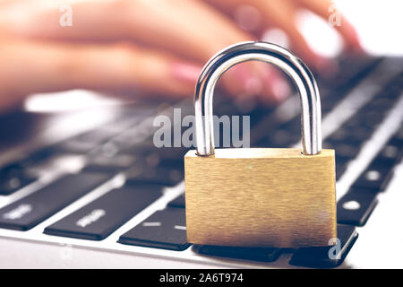 Concept of digital security and cryptology system - closed padlock on the laptop and female hands typing on a keyboard in the background Stock Photo