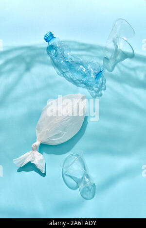 Marine waves from shadows of polyethylene foil with floating bottles, plastic fish and cups underwater on a pastel blue background, copy space. Concep Stock Photo