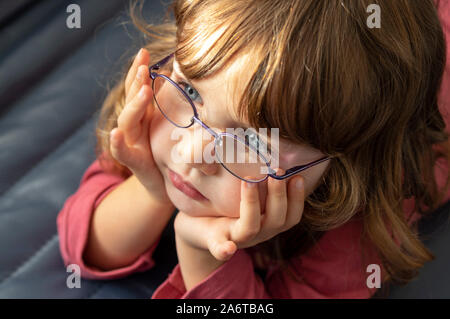 Close up portrait of a three years old blue eyed blond girl with eye glasses looking into the light. Stock Photo