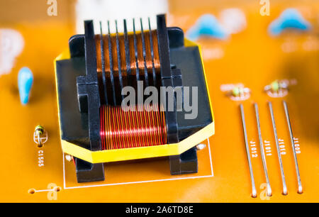 Magnetic ferrite core transformer detail on beige printed circuit board. Close-up of induction coils with copper wire winding. Electrotechnical device. Stock Photo