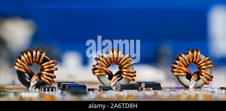 Toroidal inductors with beautiful copper wire winding. Electronic components as coils or transistors on circuit  board detail. Electrotechnical device. Stock Photo