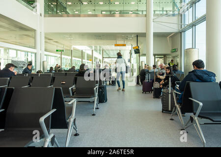 People sit on seats and wait at a departures gate in Heathrow Airport. Stock Photo